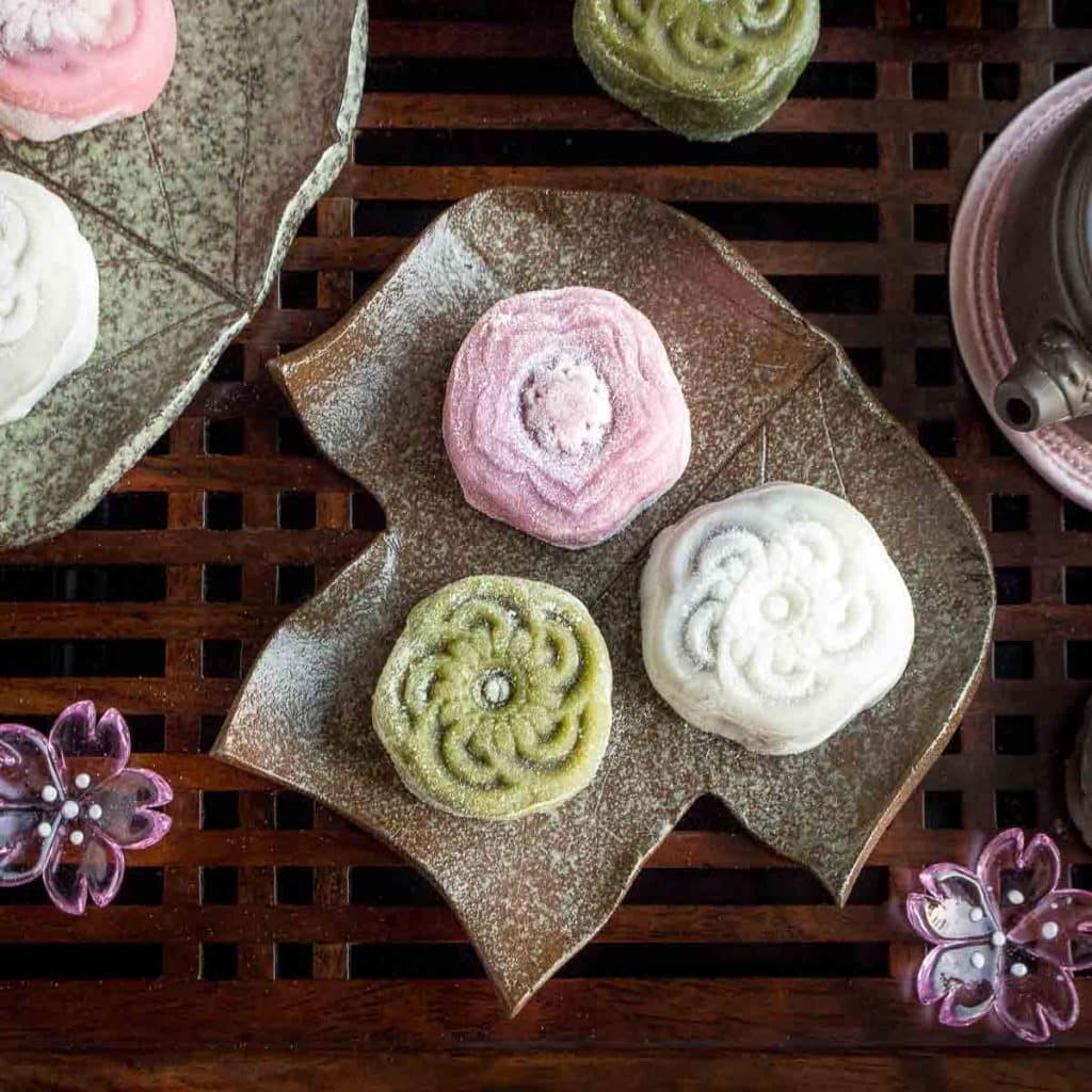 3 snow skin mooncakes colored matcha green and pink strawberry on a leaf plate.
