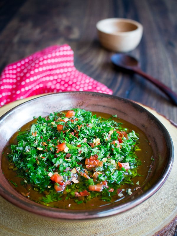 Fresh and bright chimichurri sauce in a brown plate with a red napkin with a spoon.