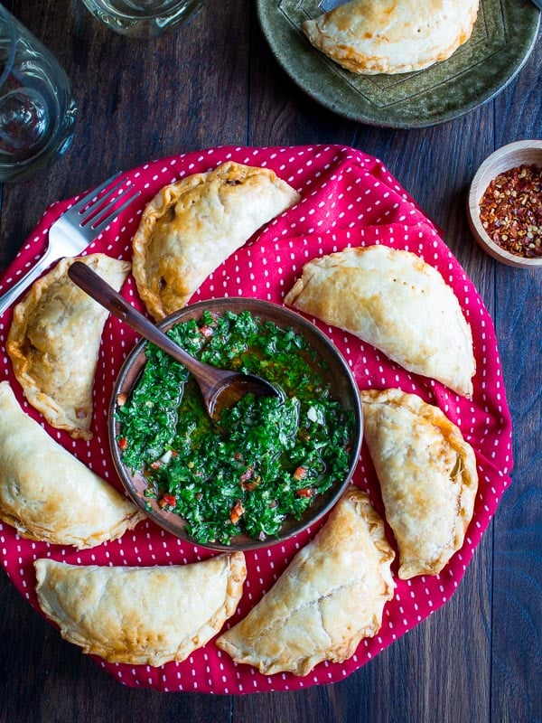 Empanada on a red plate with chimichurri sauce in the middle.
