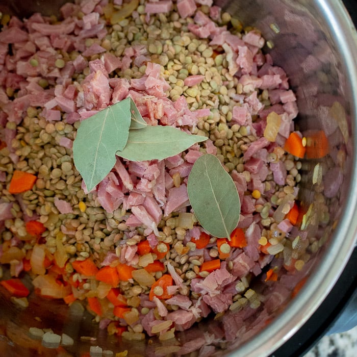 Ingredients being added to the instant pot with 3 leaves of bay leaves on the top.