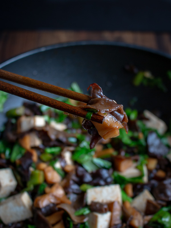 The Bite Shot of a stir fried mushroom being held by chopsticks.