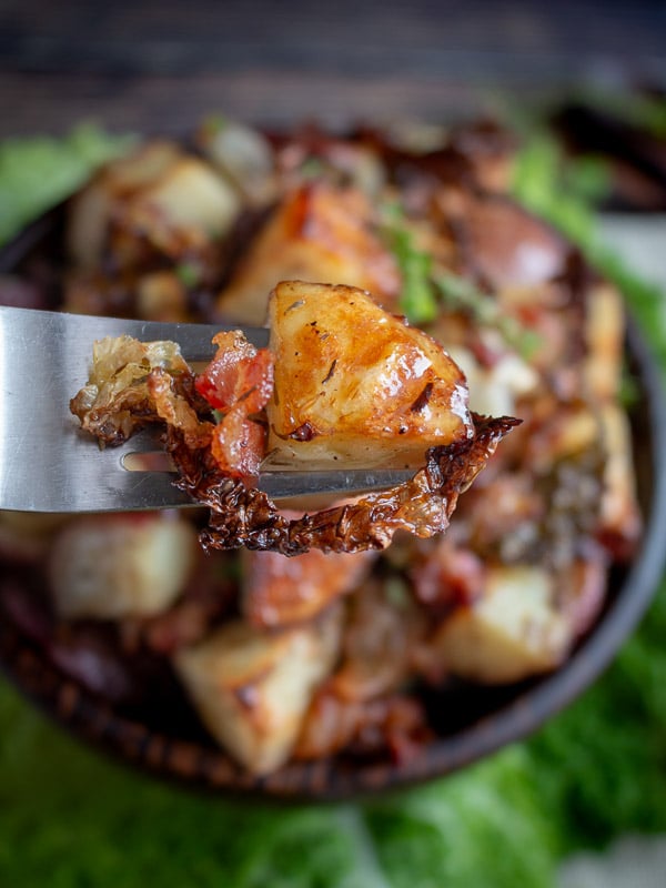 A bite of crispy potatoes, bacon and cabbage on a fork ready to eat. 