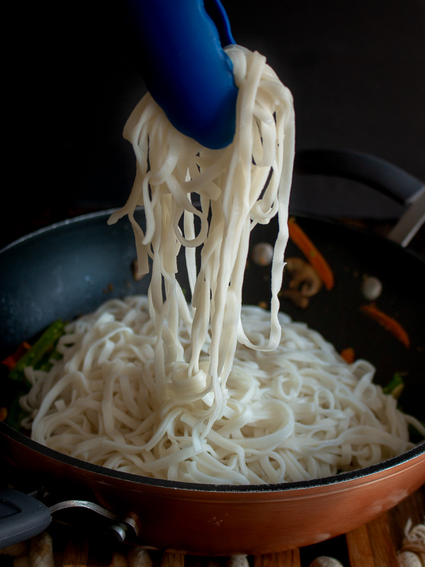 Lo mein noodles getting placed in the wok with the mixed veggies. 