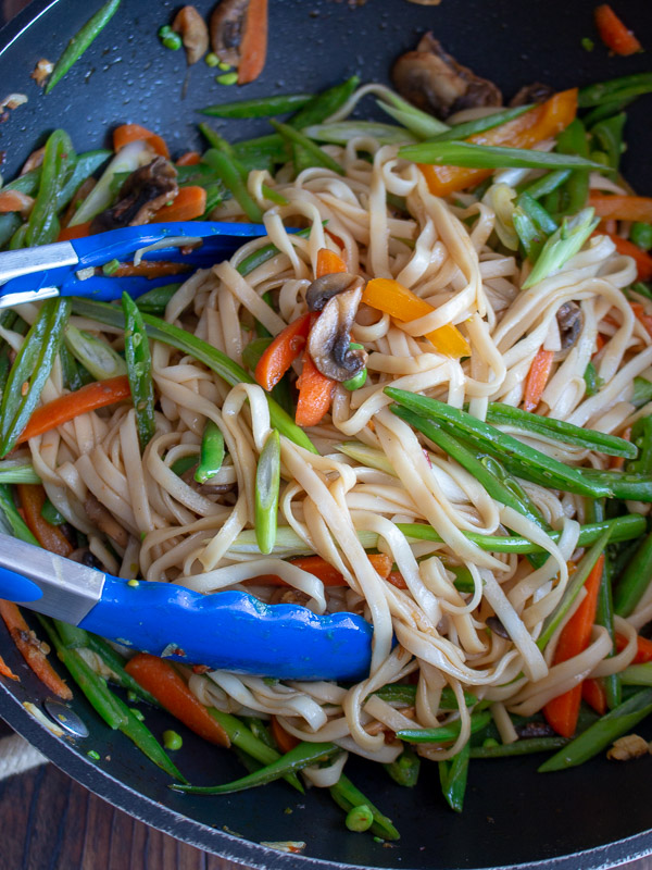 Long noodles getting mixed with with the Chinese sauce and veggies in the wok. 