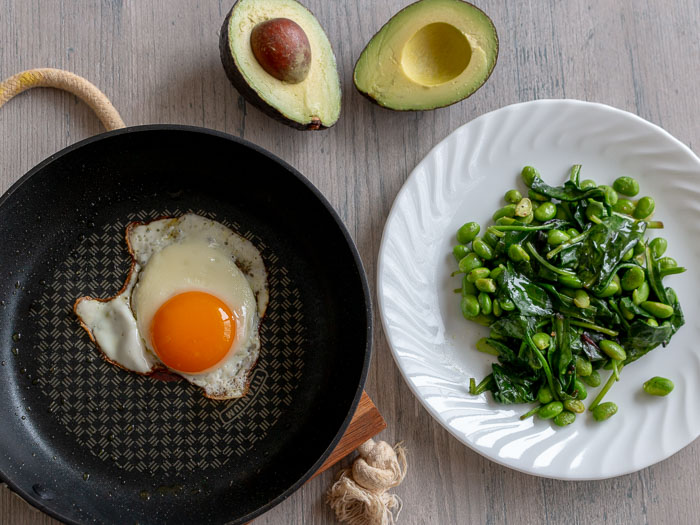 All the ingredients laid out to make a salad, cooked greens, avocado and cooked sunny side up egg.