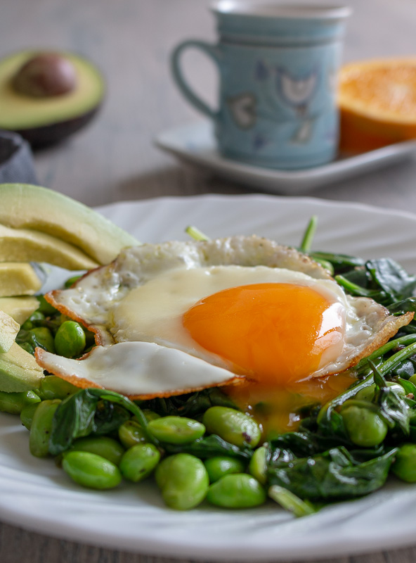 Drippy egg over the salad greens with a cup of coffee and oranges in the background.