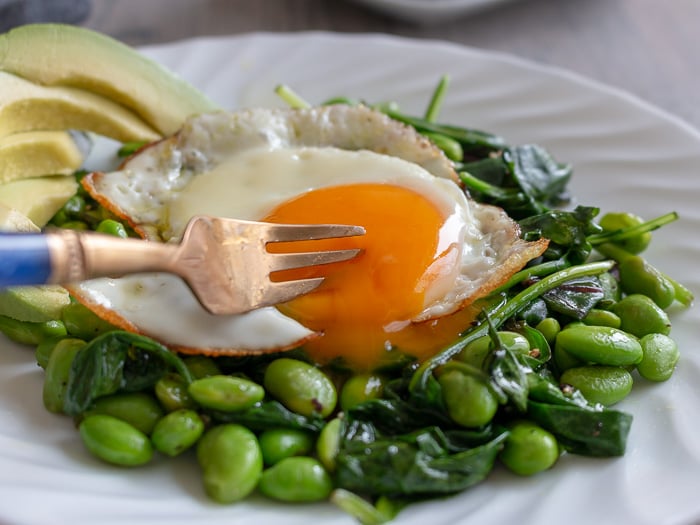 Bite shot. Fork poking a hole into the sunny side up egg. 