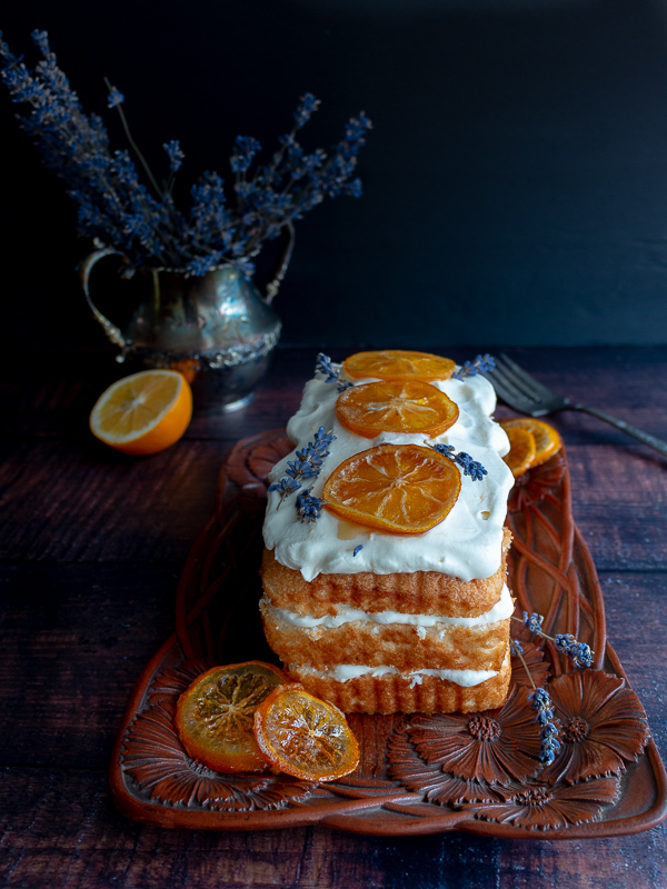 Lavender and lemon icebox cake ready to be cut topped with candied lemons and a bouquet of lavender in the background