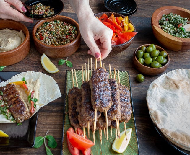 Person grabbing a lamb kabob off the entertaining table with all of the toppings for a Middle Eastern Party. 