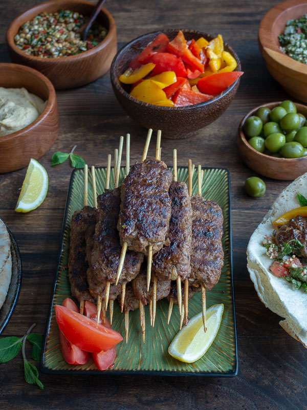 Ground lamb grilled on a stick with all the toppings nearby.