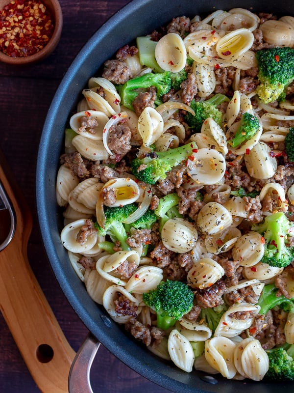 Pasta, sausage and broccoli getting tossed in a skillet.