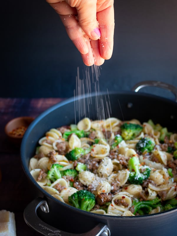  Parmesan cheese getting sprinkled on top of pasta.