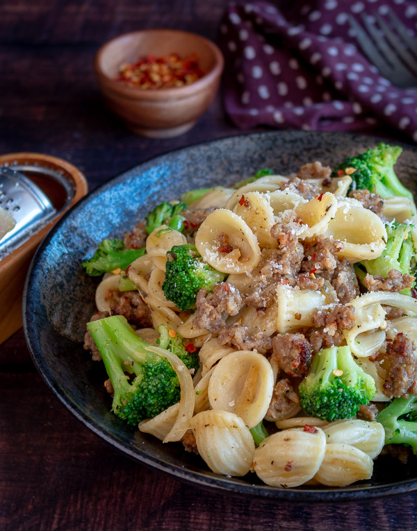 Orecchiette and Chicken Sausage in a Garlic Wine Sauce topped with parmesan cheese and red pepper flakes in the back ground.