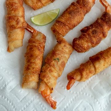 5 Thai Firecracker Shrimp appetizers laying a a lined white plate with limes.