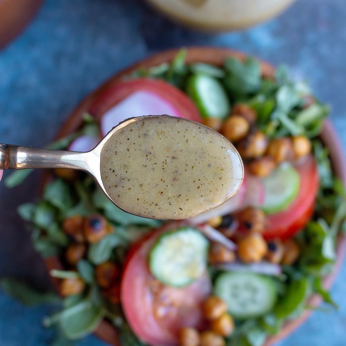 Salad dressing in a spoon held over a tossed salad.