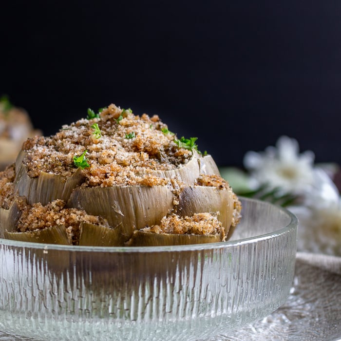 Closeup shot of cooked breaded stuffed artichokes sprinkled with a little extra parmesan and fresh parsley in a glass bowl.