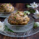 2 gigantic globe artichokes stuffed and steamed in glass bowls with white flowers around the bowls.