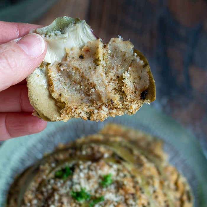 One artichoke leaf peeled off the whole artichoke showing the stuffing inside and the tender artichoke. 