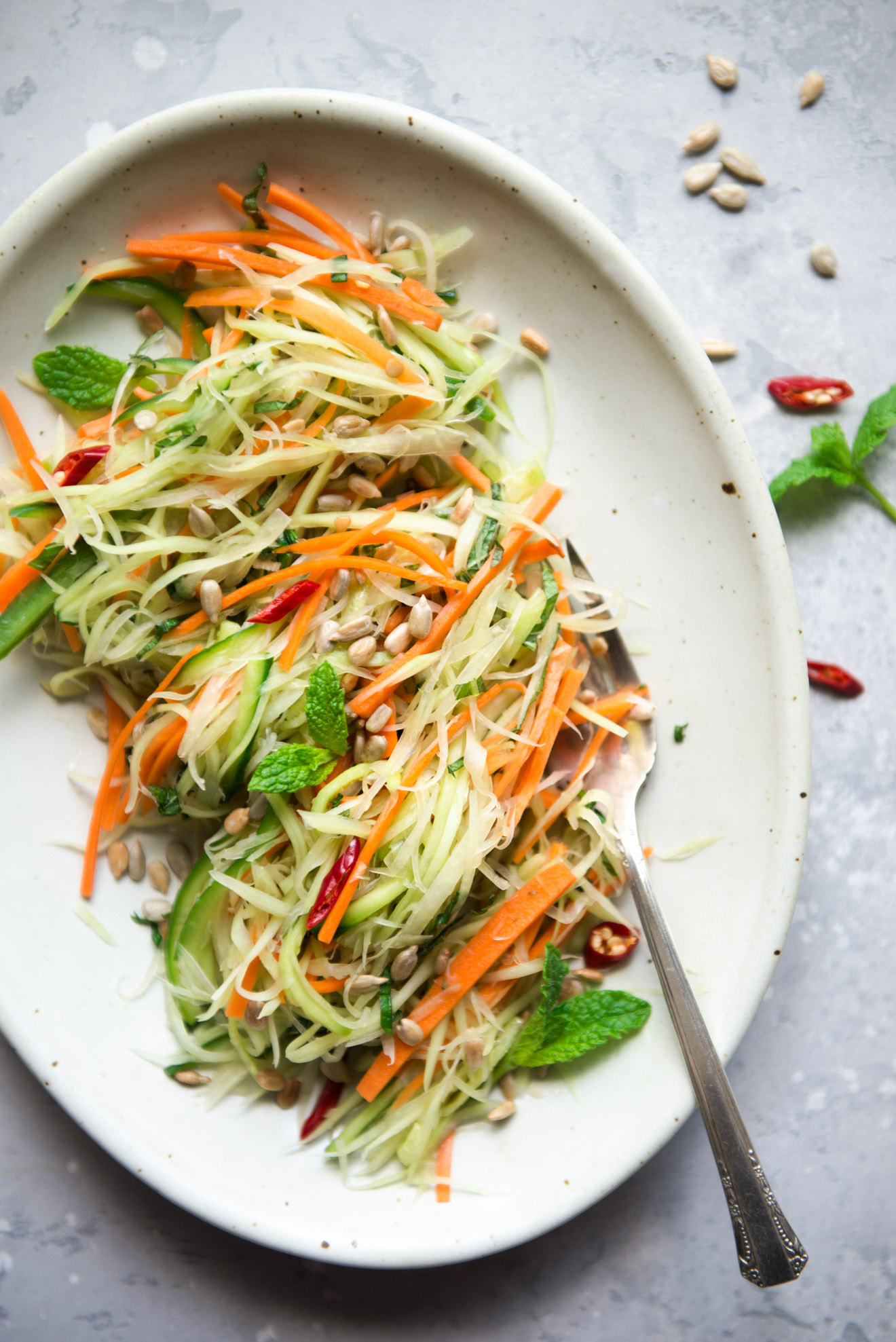 Vegan green papaya salad garnished with sunflower seeds, mint and chili