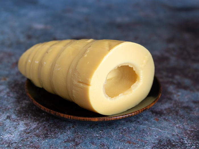 Fresh whole bamboo shoot that has been peeled and boiled on a black plate and blue back ground. 