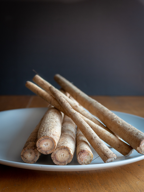 Whole burdock root 8 stalks on a white plate.