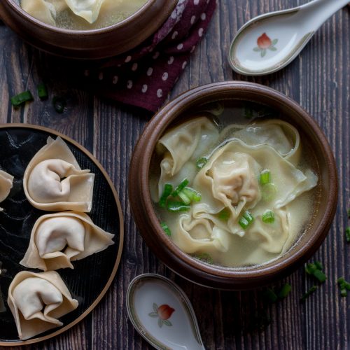 Shanghai Wonton Soup with a plate of wontons to be cooked next to it and 2 spoons.