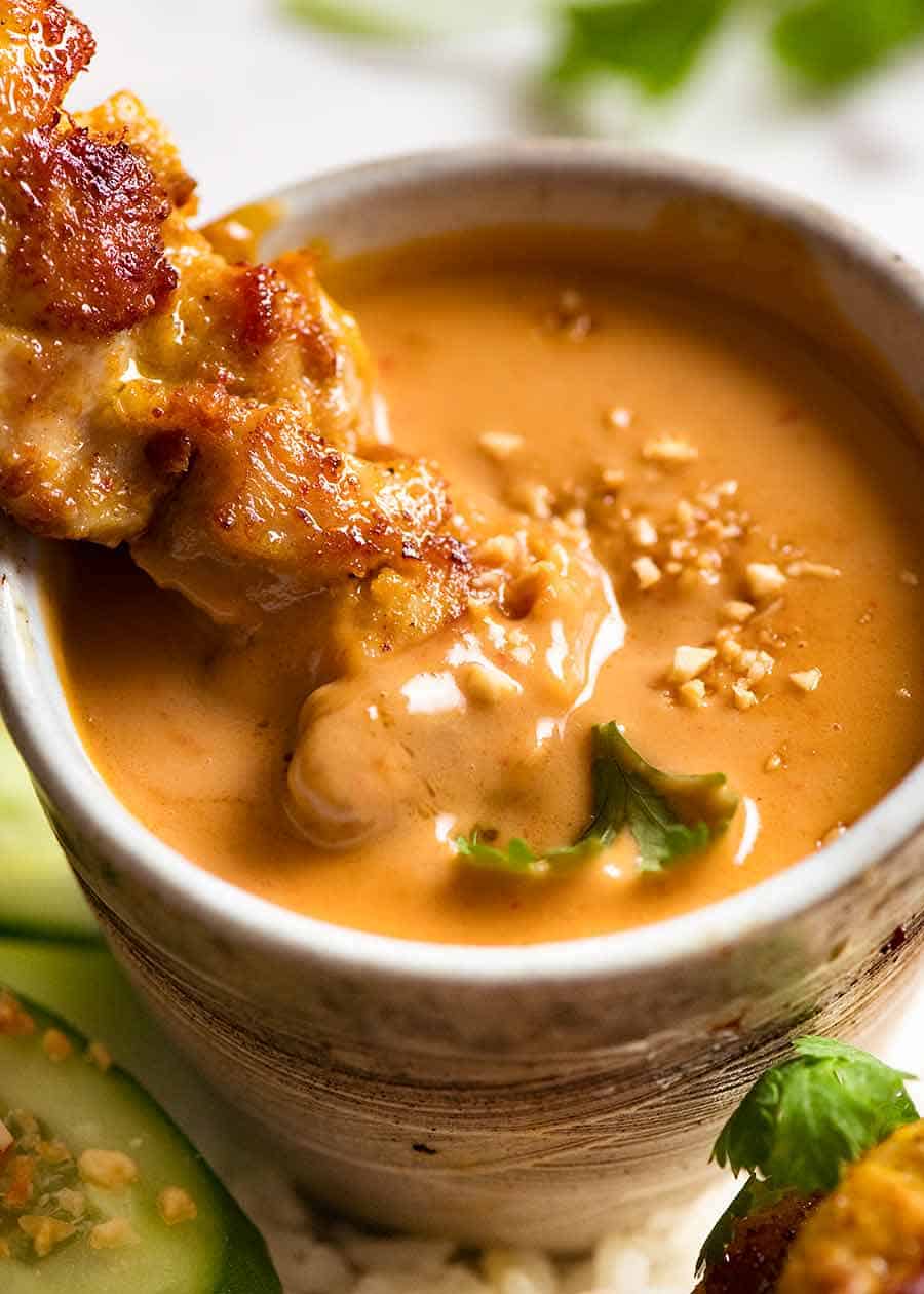 Chicken Satay on a skewer dipping into a bowl of peanut sauce.