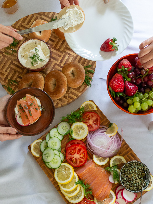 Friends gathering around the Ultimate Bagel brunch board and digging in.