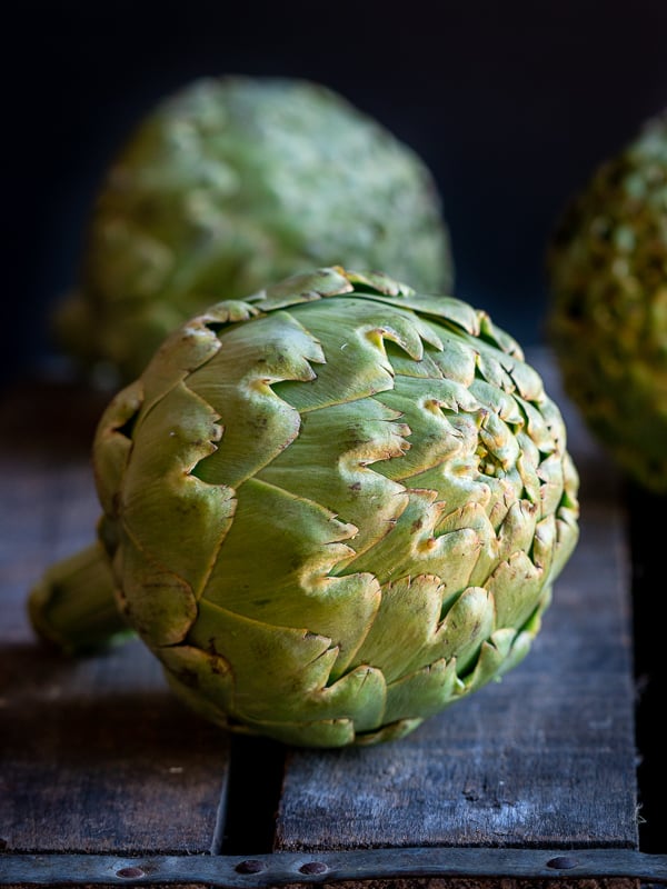 3 whole globe artichokes on a wooden crate fresh from the farmers market.