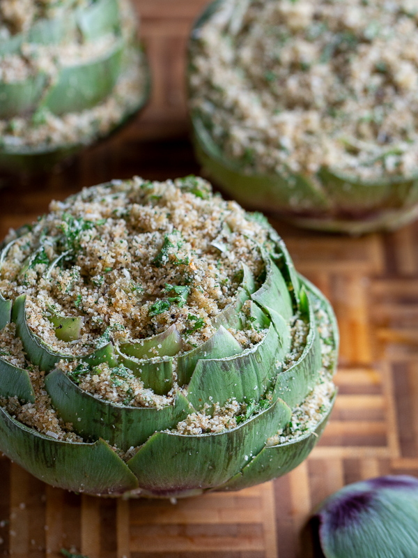 3 stuffed artichokes on a bamboo cutting board ready to be steamed.