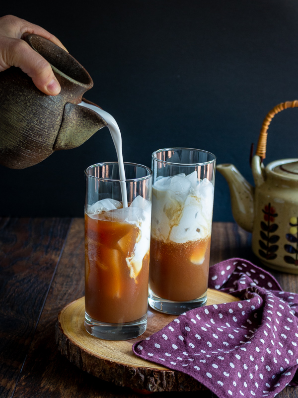 Coconut milk getting poured into each glass that is ¾ of the way filled with date sweetened Masala Chai Tea.