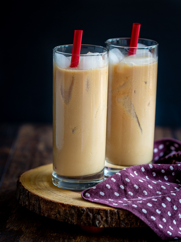 Two glasses of mixed Easy Coconut Iced Chai Tea with ice and red straws on a wooden serving platter.