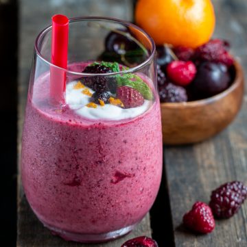 Berry Cherry Smoothie Blast in a glass with a red straw and topped with berries and coconut cream.