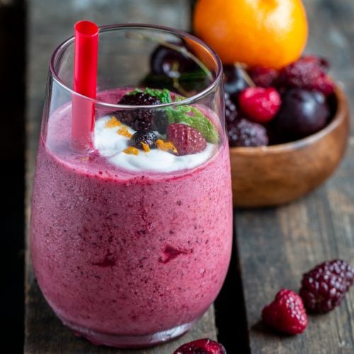 Berry Cherry Smoothie Blast in a glass with a red straw and topped with berries and coconut cream.