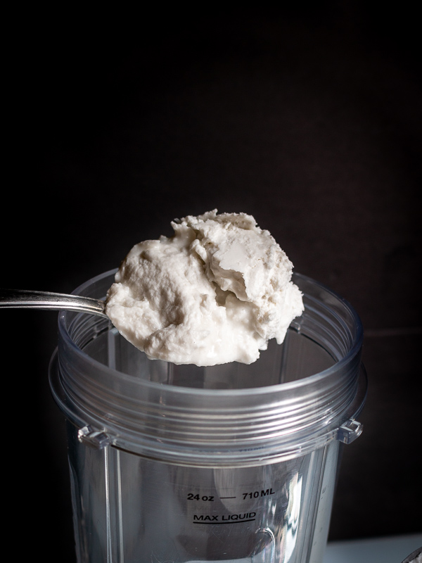 Placing a large scoop of the coconut cream solids into the chilled food processor container.