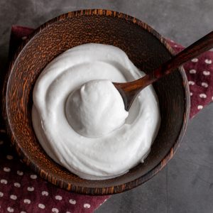 Top down photo of creamy dreamy coconut whipped topping in a brown wooden bowl with a dollop in a wooden spoon.