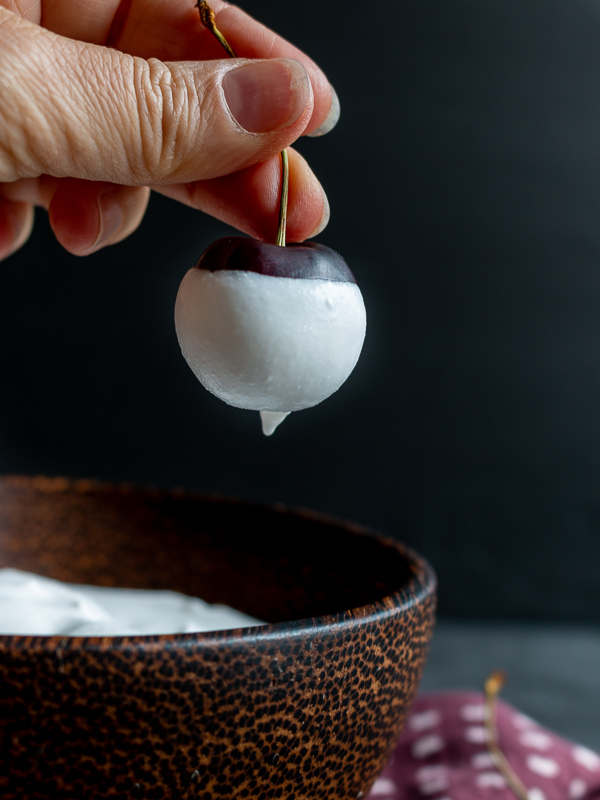 Sweet michigan cherry dipped in a little creamy homemade whipped coconut cream held over a bowl of topping.