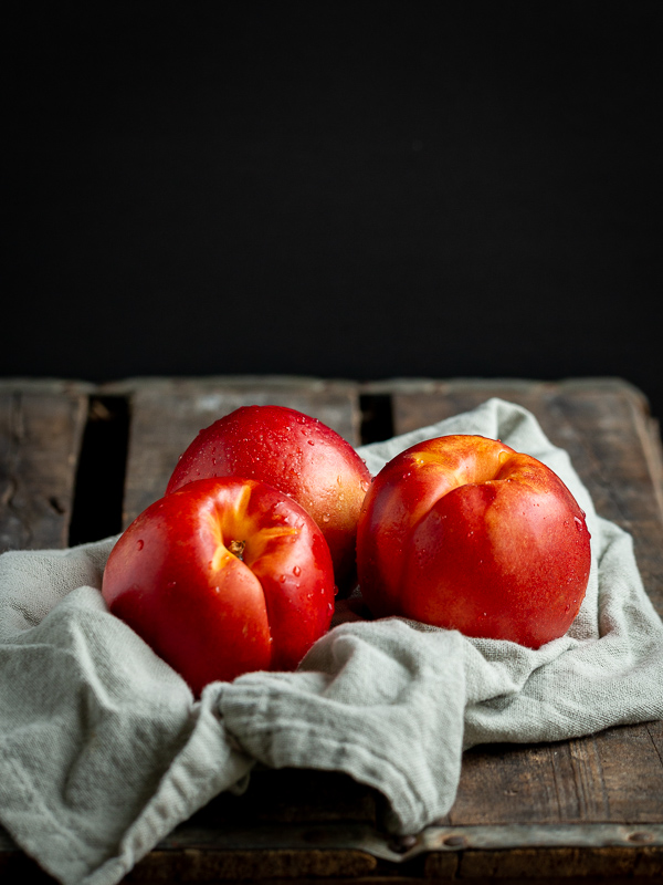 3 ripe nectarines on a wooden box on a light green tea towel.