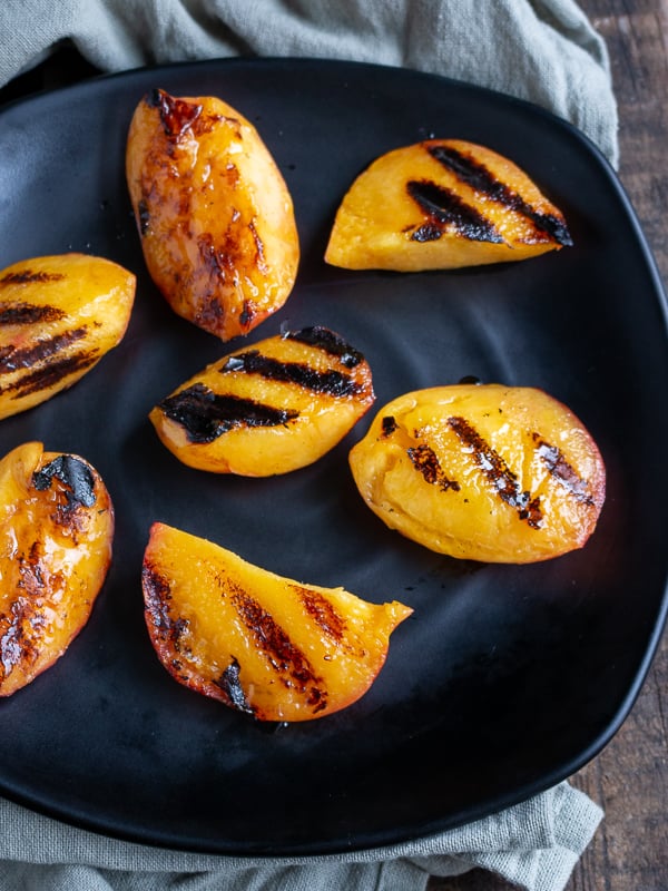 Nectarines with perfect grill marks on a black plate.