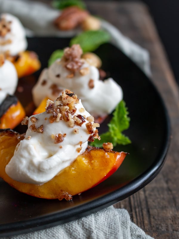Close up shot. Grilled Nectarines with a dollop of whipped coconut cream and crushed candied nuts on each.