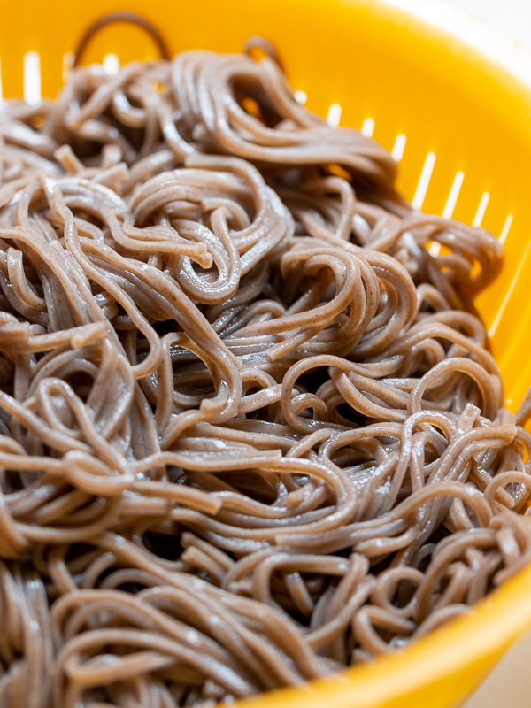 Cooked and rinsed soba noodles in a yellow colander.