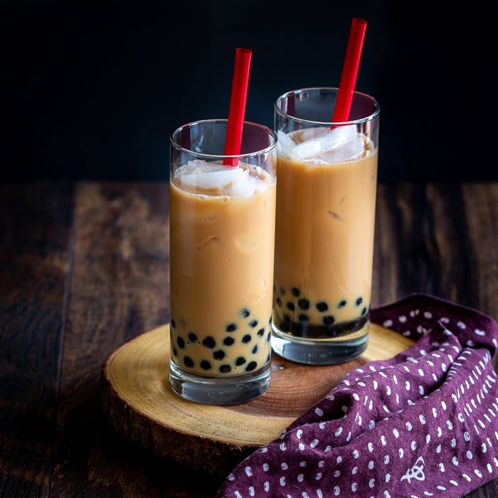 2 glasses of bubble tea with red straws on a wooden board.