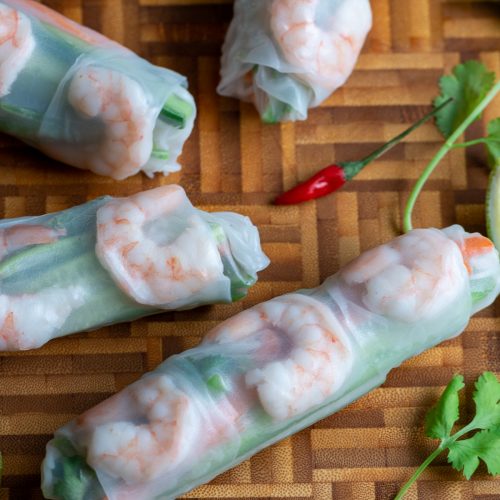 4 summer rolls with a bowl of chili lime sauce on a cutting board.