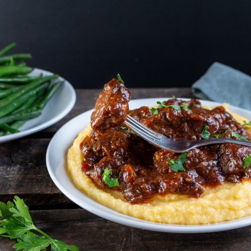 Tuscan Slow Cooked Braised Beef in Wine Sauce on a bed a creamy polenta with a bite ready for you.