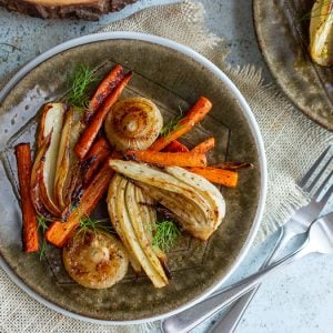 Roasted fennel, carrots and onions on a green plate garnished with green tops of fennel.