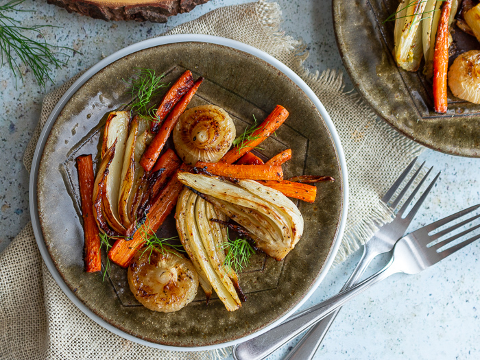 Roasted fennel, carrots and onions on a green plate garnished with green tops of fennel.