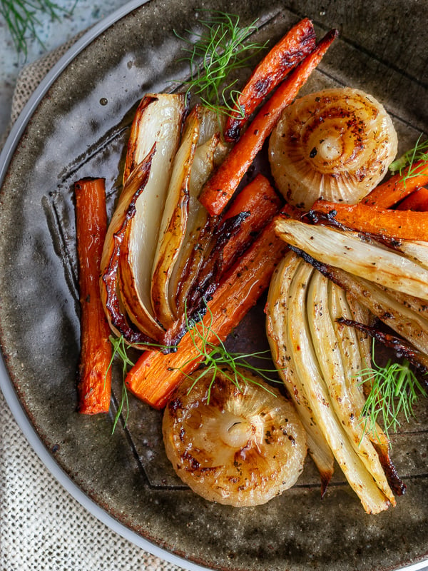 Top down shot of balsamic roasted fennel and carrots with swirly green frangs to garnish.