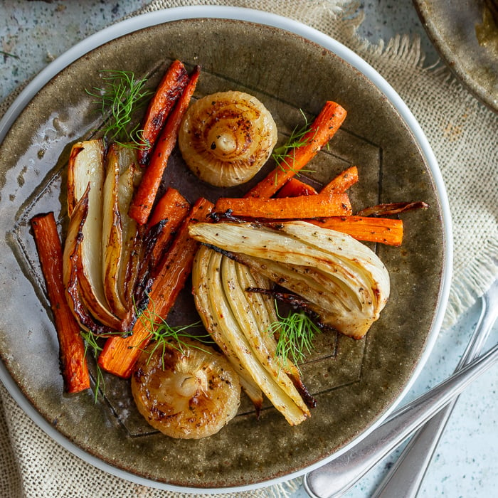 Roasted fennel, carrots and onions on a green plate garnished with green tops of fennel.