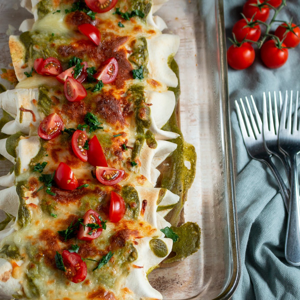 Tray of shrimp Burritos with poblano sauce topped with tomatoes and cilantro.