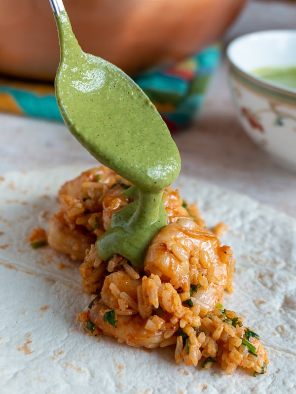 Creamy poblano sauce getting spooned over the shrimp and rice mixture on a tortilla.